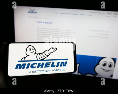 Person, die ein Mobiltelefon mit dem Logo der Compagnie Générale des établissements Michelin SCA vor der Business-Webseite hält. Schwerpunkt auf dem Display des Telefons. Stockfoto