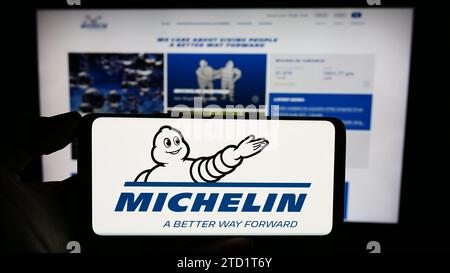 Person, die ein Mobiltelefon mit dem Logo der Compagnie Générale des établissements Michelin SCA vor der Webseite hält. Schwerpunkt auf dem Display des Telefons. Stockfoto