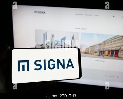 Person, die ein Smartphone mit dem Logo der österreichischen Immobiliengesellschaft Signa Holding GmbH vor der Website hält. Schwerpunkt auf dem Display des Telefons. Stockfoto