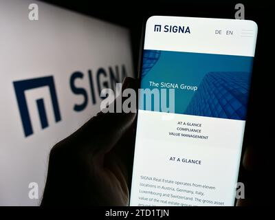 Person mit Mobiltelefon und Website der österreichischen Immobiliengesellschaft Signa Holding GmbH vor dem Logo. Konzentrieren Sie sich auf die Mitte des Telefondisplays. Stockfoto