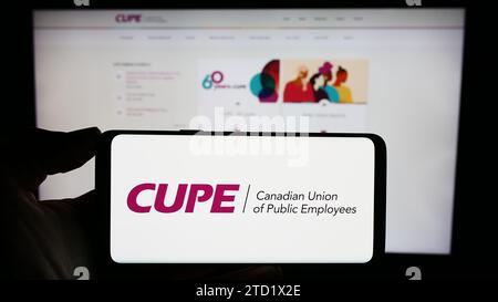 Person, die ein Mobiltelefon mit dem Logo der gewerkschaft Canadian Union of Public Employees (CUPE) vor der Unternehmenswebseite hält. Schwerpunkt auf dem Display des Telefons. Stockfoto