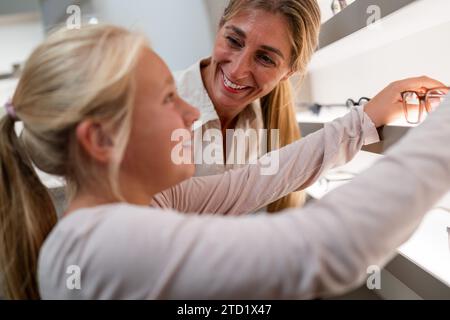Das Kind greift nach einer Brille im Regal, während ein Erwachsener im optischen Geschäft eine neue Brille kauft Stockfoto