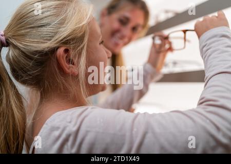 Das Kind greift nach einer Brille im Regal, während ein Erwachsener im optischen Geschäft eine neue Brille kauft Stockfoto