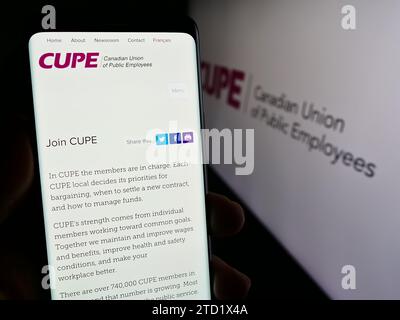 Person mit Smartphone und Website der gewerkschaft Canadian Union of Public Employees (CUPE) mit Logo. Konzentrieren Sie sich auf die Mitte des Telefondisplays. Stockfoto