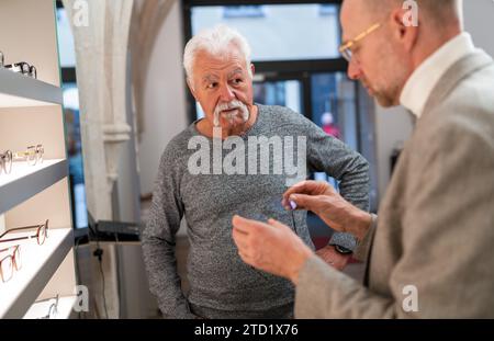 Senior Mann, der einem Optiker zuhört, der ein neues Brillenmodell in der Hand hält Stockfoto