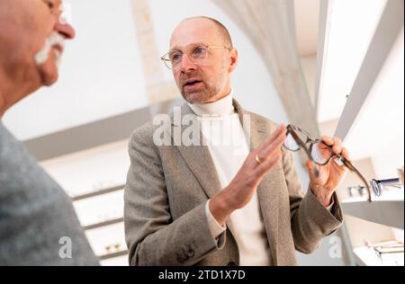 Optiker diskutiert Brillen mit Senior männlichen Kunden im Geschäft. Er zeigt auf die Brille. Stockfoto