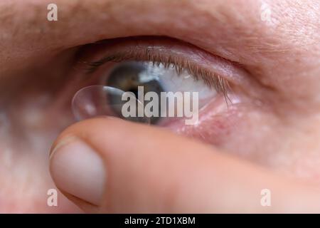 Makroaufnahme eines Auges mit Kontaktlinse am Finger. Stockfoto