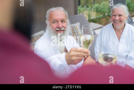 Seniorenpaar in weißen Bademänteln, die Champagner von einem Kellner in einem Wellnesshotel erhalten. Bild des Konzepts zum Geburtstag und Valentinstag Stockfoto