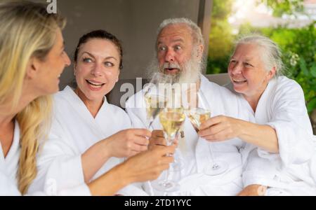 Zwei Frauen und ein Seniorenpaar lachen und toasten mit Sektgläsern in einem Wellnesshotel Stockfoto