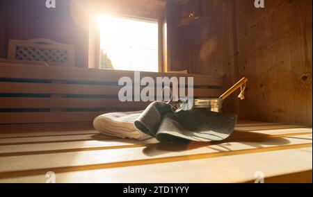 Sauna-Innenraum mit Filzhüten, Handtüchern, Kelle und Eimer, Sonnenlicht durch Fenster in einer finnischen Sauna. Konzept Spa Wellness Hotel. Stockfoto