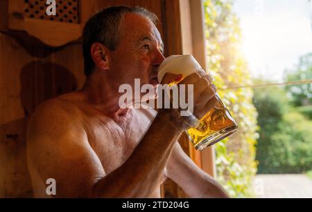 Mann trinkt deutsches Bier in der bayerischen Sauna, Sonnenlicht durch das Fenster. Spa Wellness Hotel Konzept Bild Stockfoto