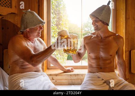 Glückliche deutsche Männer in der finnischen Sauna mit Filzhüten, die mit dem Becher getoastet werden. Hotel Spa okotoberfest Konzeptbild Stockfoto