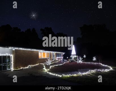 Kleines Bauernhaus mit allen weißen Lichtern, die den Hof während der Feiertage dekorieren, mit einem hellen Stern, der am Heiligabend am Himmel aufsteigt Stockfoto