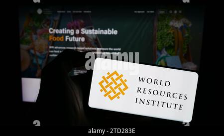 Person, die ein Mobiltelefon mit dem Logo der Forschungsorganisation World Resources Institute (WRI) vor der Webseite hält. Schwerpunkt auf dem Display des Telefons. Stockfoto