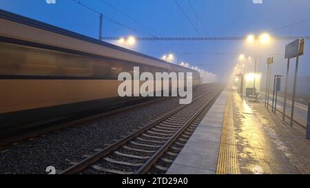 Nachtzug im Nebel. Station in Nebel und Dunkelheit. Die Fahrt des Expresszuges in Nebel und Dunkelheit. Das Konzept der Verkehrsprobleme, der Vorortverkehr Stockfoto