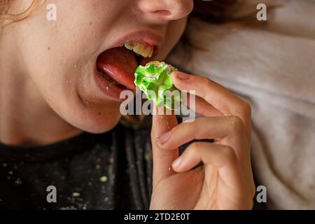 Glückliches Mädchen im Teenageralter, das auf dem Sofa liegt und süßen Zucker, bunte Marmeshow isst Stockfoto