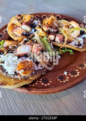 Köstliches Gericht von Sopes und Seafood Tostadas, eine gebratene Tortilla mit Bohnen, Garnelen und Oktopus darauf Stockfoto