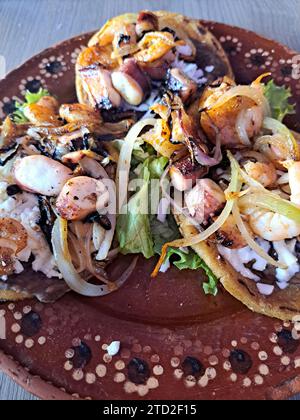 Köstliches Gericht von Sopes und Seafood Tostadas, eine gebratene Tortilla mit Bohnen, Garnelen und Oktopus darauf Stockfoto