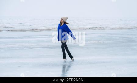 Eine weiße Frau in einem blauen Pullover läuft auf einem gefrorenen See. Der Eiskunstläufer führt das Programm aus. Stockfoto