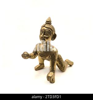 Goldene Vintage-Figur des krabbelnden Baby-Lord krishna, auch gopal genannt, mit süßem Laddu in der Hand isoliert auf einem weißen Hintergrund Stockfoto