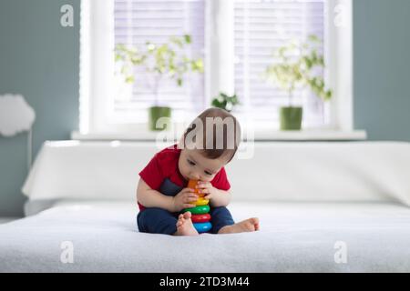 Kleiner barfuß Junge im roten T-Shirt, der seine Lieblingsspielzeug-farbige Pyramide isst. Das Konzept der glücklichen Kindheit Stockfoto