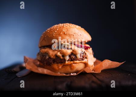 Appetitlicher schlampiger Cheeseburger auf Pergamentpapier auf Holztisch. Lebensmittelfotografie Stockfoto