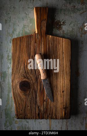 Kleines Messer mit Holzgriff, das auf einem alten Schneidebrett auf einem rostigen alten Tisch liegt Stockfoto