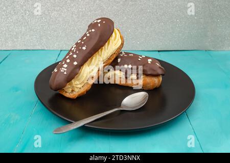 Zwei Eclair-Kuchen auf einer schwarzen Keramikplatte und blauer Holzbretttisch Stockfoto