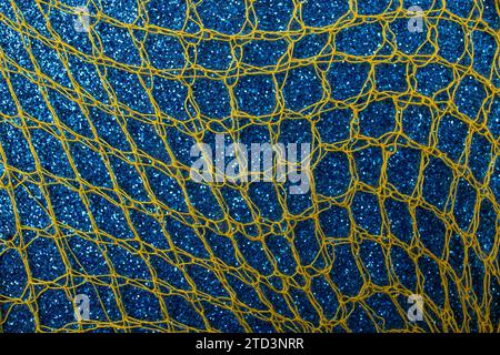 Gelbes Fischnetz auf blauem Glitzer-Hintergrund, abstrakter Texturhintergrund, weicher Fokus Stockfoto