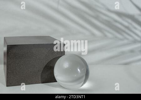 Leerer grauer Hintergrund mit einem Würfel und einer Glaskugel auf einem grauen Hintergrund mit Palmen hinterlässt Schatten, weicher Fokus Stockfoto