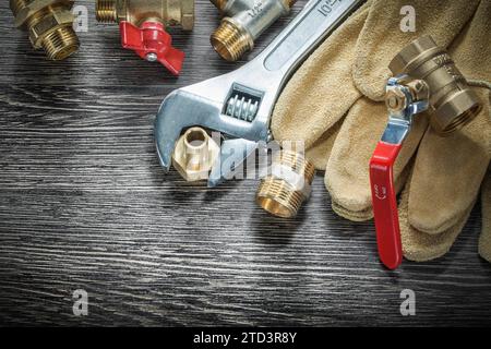 Verstellbarer Schraubenschlüssel Wasserventil Rohrverschraubungen Leder-Sicherheitshandschuhe auf Holzbrett Stockfoto