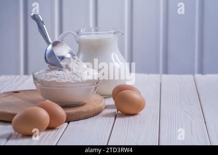 Kompositionsschüssel mit Mehl scop Eier Milch im Krug auf weiß lackiertem altem Holzbrett Lebensmittel- und Getränkekonzept Stockfoto