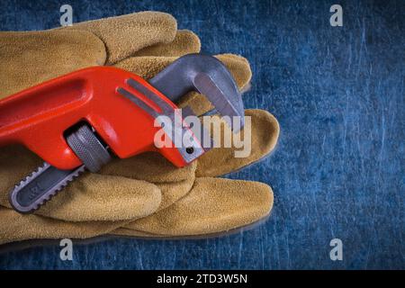 Neuer roter Affenschlüssel mit Lederhandschuhen auf zerkratzter metallischer Oberfläche Stockfoto