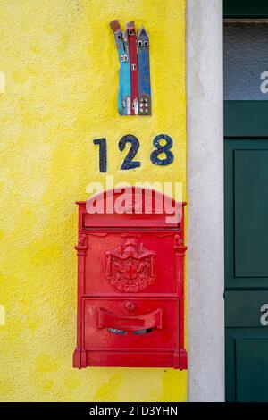 Roter künstlerischer Briefkasten auf einer gelben Hauswand mit Hausnummer, farbenfrohe Häuser auf der Insel Burano, Venedig, Veneto, Italien Stockfoto