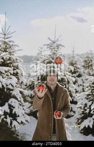 Mann in einer verschneiten Landschaft, der mit roten Weihnachtskugeln jongliert Stockfoto