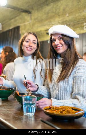 Vertikales Foto von zwei stilvollen Frauen, die Ramen-Suppe in einem Restaurant essen Stockfoto