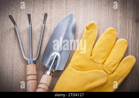 Nahaufnahme einer Gartenkelle aus Stahl mit Handspaten und Ledersicherheitshandschuhen auf Holzbrett Landwirtschaftskonzept Stockfoto