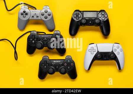 Verschiedene Generationen von Gamecontrollern der PlayStation-Spielekonsole, ab Modell 1-5 vor glanzgelbem Hintergrund, Draufsicht Stockfoto