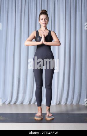 Bild einer schönen Frau in einem schwarzen Turnanzug, die auf einem Sadhu-Brett in einem hellen Studio steht. Yoga-Konzept. Spirituelle Praktiken. Nageln. Gemischt Stockfoto