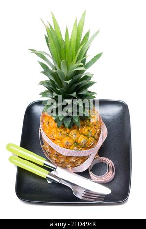 Ananas auf einem schwarzen Teller mit Bandmesser, Messer und Gabel isoliert auf weißem Hintergrund, Lebensmittelfotografie Stockfoto