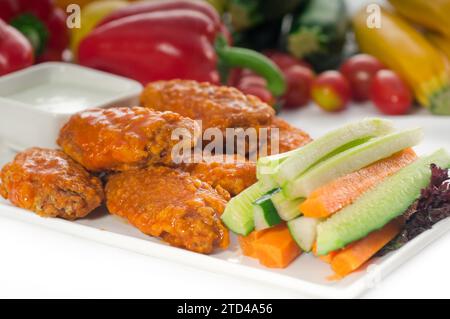 Klassische Buffalo Chicken Wings serviert mit frischem Pinzimonio und Gemüse im Hintergrund, KÖSTLICHERE SPEISEN IM PORTFOLIO, Lebensmittelfotografie Stockfoto