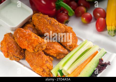 Klassische Buffalo Chicken Wings serviert mit frischem Pinzimonio und Gemüse im Hintergrund, KÖSTLICHERE SPEISEN IM PORTFOLIO, Lebensmittelfotografie Stockfoto