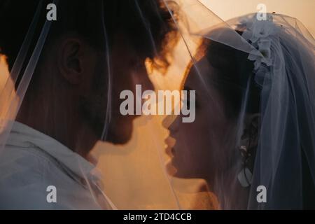 Wunderschönes junges Paar, verliebt, frisch vermähltes Paar unter einem Schleier, Liebesgeschichte bei Sonnenuntergang Stockfoto