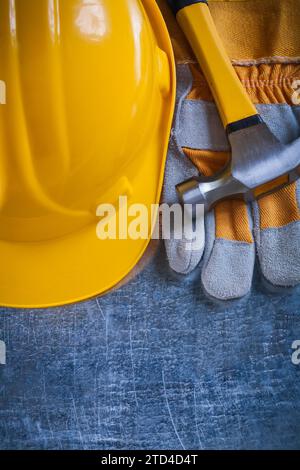 Schutzhandschuhe gelber Bauhelm und Metallkrallenhammer auf zerkratztem metallischem Hintergrund Wartungskonzept Stockfoto