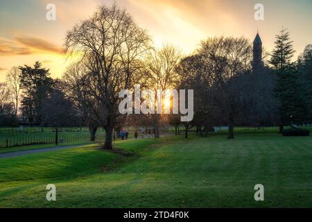 Menschen gehen und joggen auf dem Fußweg im Farmleigh Phoenix Park bei schönem Sonnenuntergang mit Sonnenlicht durch Bäume, Dublin, Irland Stockfoto