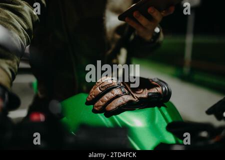 Ein brauner Lederhandschuh liegt auf dem Tank eines grünen Motorrads, während der Motorradfahrer auf die Route blickt Stockfoto