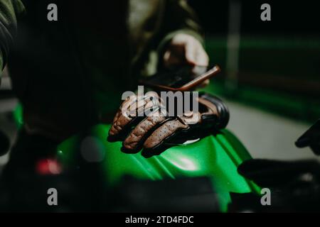 Ein brauner Motorradhandschuh aus Leder liegt auf dem Tank eines grünen Motorrads Stockfoto