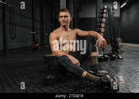 Pause nach hartem Crossfit-Training. Porträt eines jungen Sportmannes mit Flaschenauflage im Fitnessstudio nach dem Training. Stockfoto