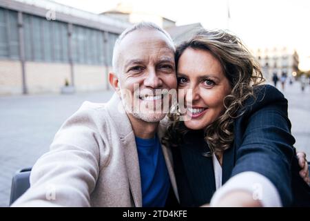 Ein liebevolles, glückliches Paar mit mittlerem Erwachsener, das Spaß hat, gemeinsam ein Selfie-Porträt auf der Straße zu machen. Mann und Frau mittleren Alters, die lächelnd anschauen Stockfoto