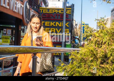 Die junge türkische Frau läuft, während sie ihr Smartphone in der Nähe des teknik Servis Ladenschilds ansieht. Ankara Türkei Stockfoto